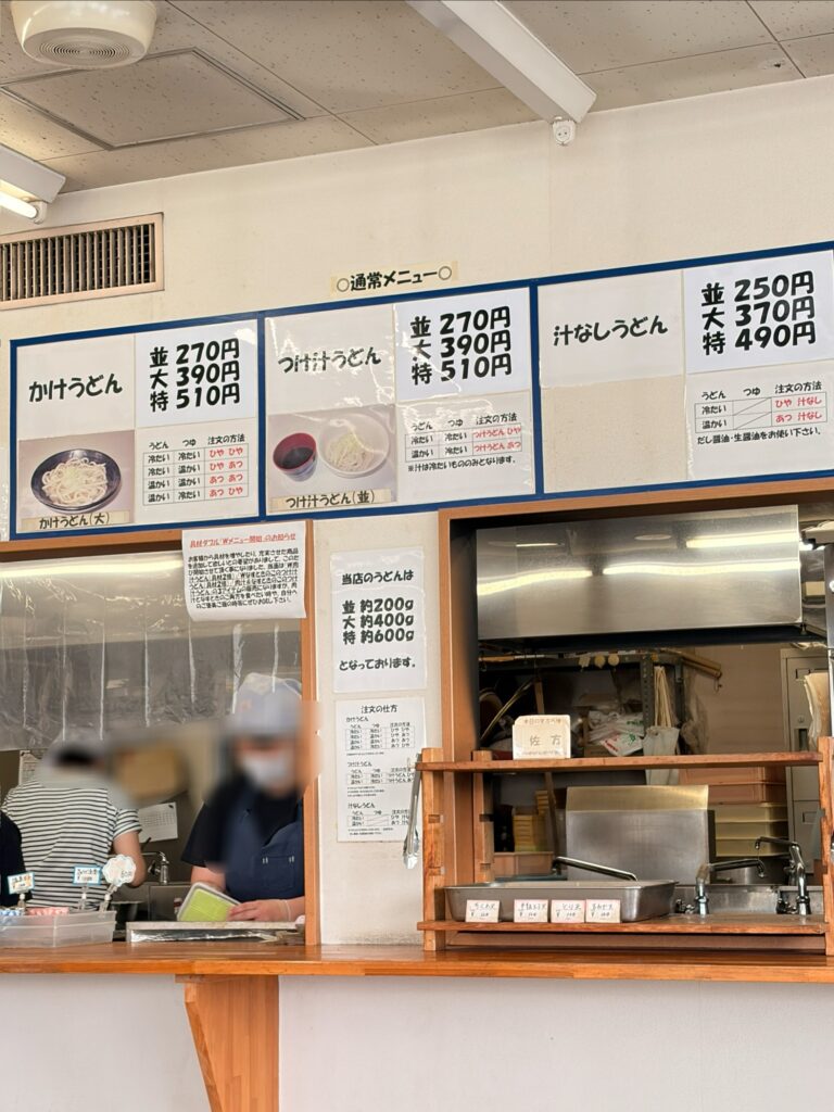安藤製麺の券売機まわりのメニュー。かけ・つけ汁・汁なしうどんの並大特の価格表