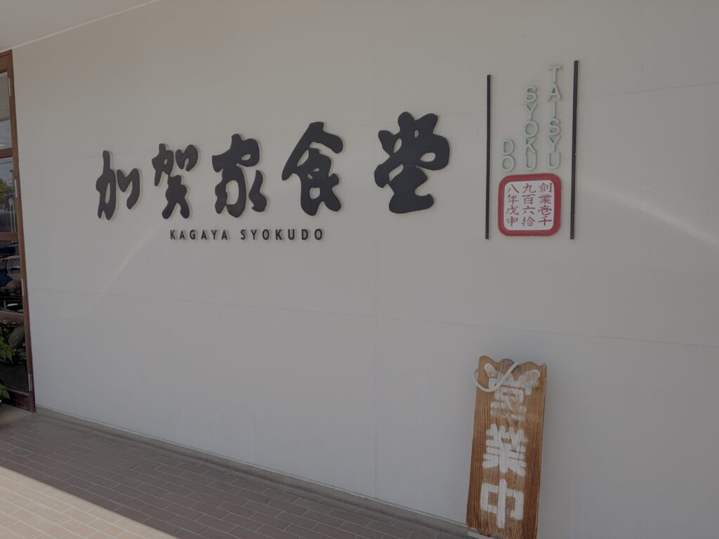 加賀家食堂の壁面ロゴ看板。「KAGAYA SYOKUDO」と創業壱千九百六拾八年戊申の文字