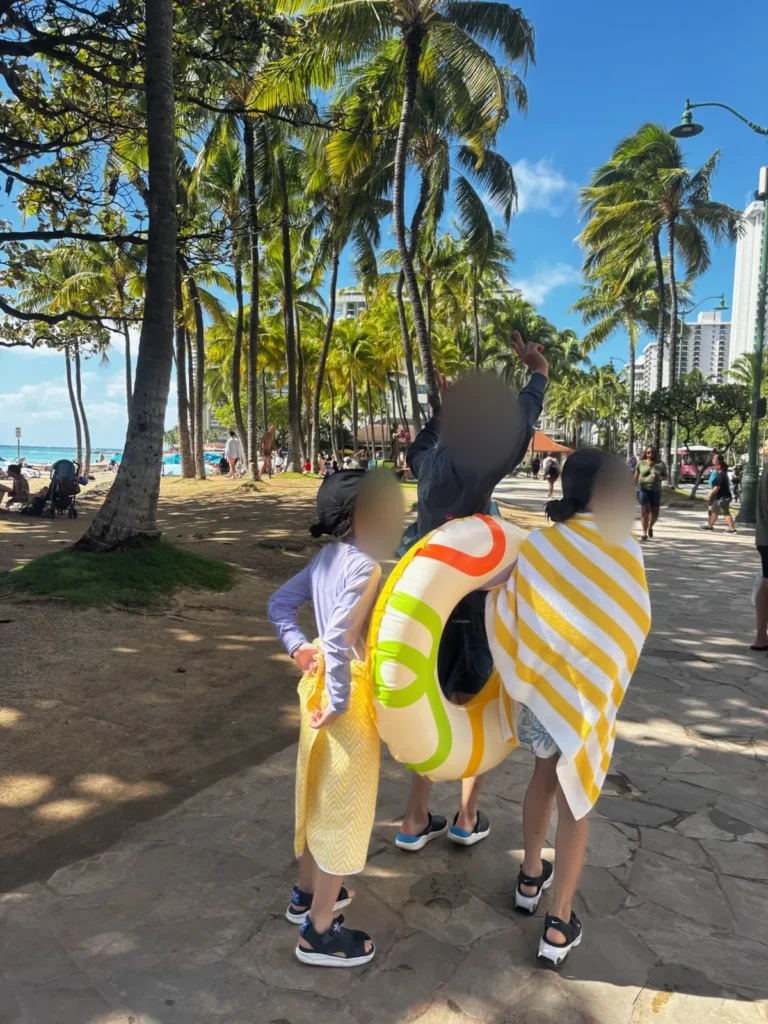 ワイキキビーチから浮き輪とタオルを持って歩く子ども達の後ろ姿