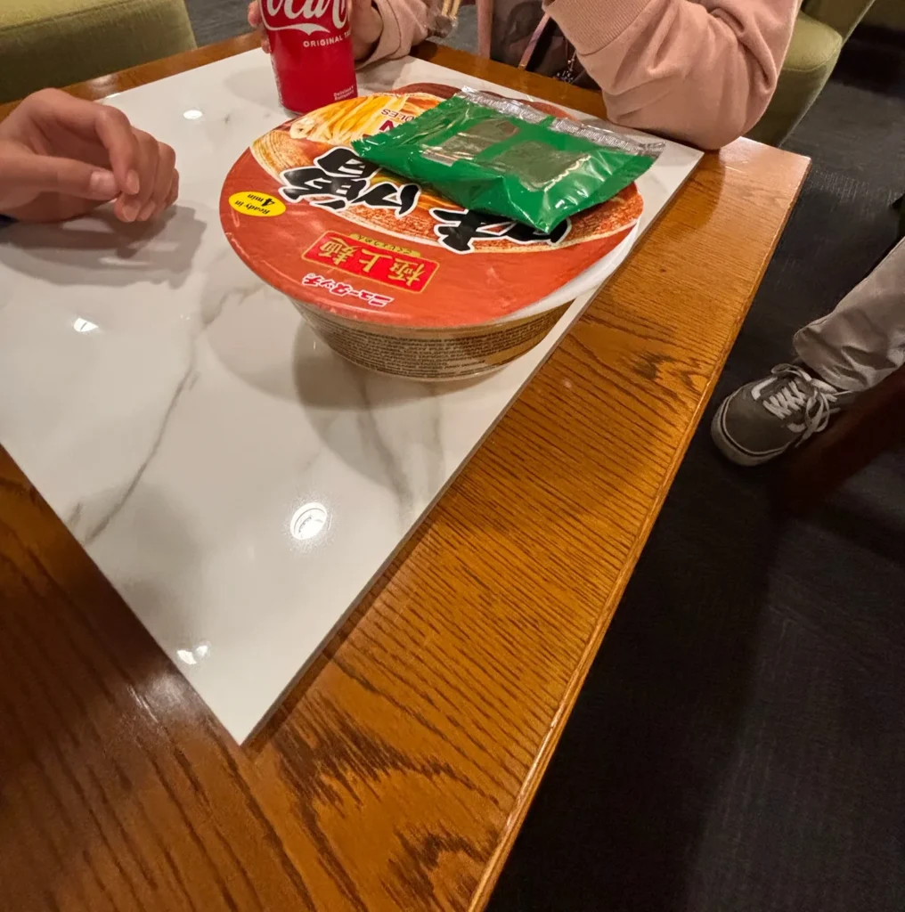 空港ラウンジのテーブルに置かれたカップの味噌ラーメンとコーラ